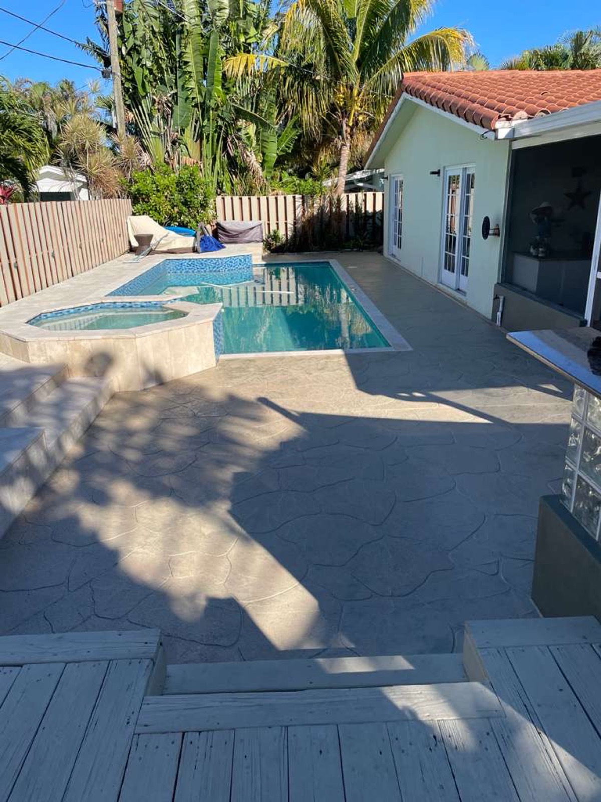 Completed New Season Designs pool deck resurfaced in a light stone finish, with the home and palm trees behind it