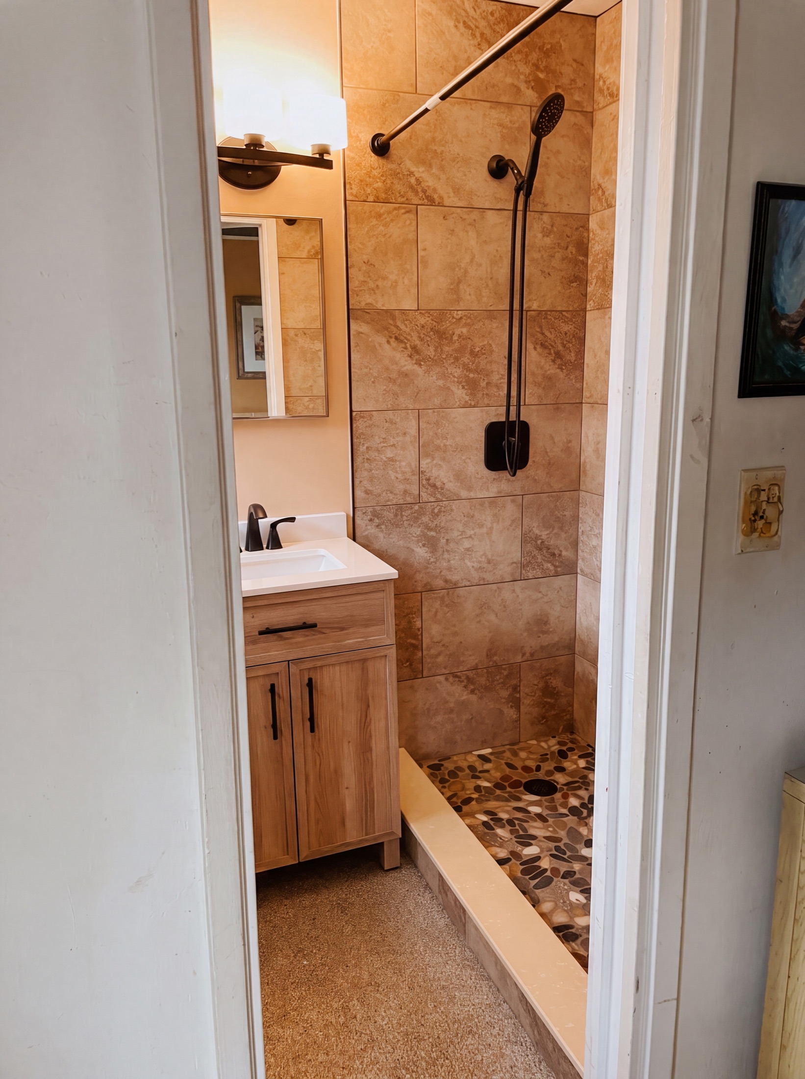 Bath after — travertine-look walk-in shower with pebble-stone floor